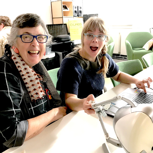 Two people smiling at the viewer over a table, one holding a 3D force-feedback joystick